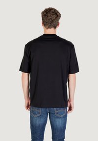 T-shirt in cotone nero con maniche corte, collo rotondo e vestibilità rilassata. Indossato con jeans in denim blu dotati di tasche posteriori e dettagli cuciti.