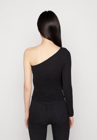 Top negro de canalé con un diseño asimétrico que deja un hombro descubierto y una manga larga, fabricado en material elástico.