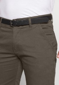 Calças de algodão verde-escuro com um cinto de couro preto texturizado. Apresenta bolsos laterais e um design slim fit. Os detalhes incluem passantes para cinto e costuras.