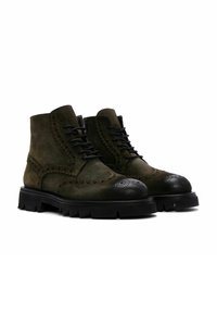 Botas de tobillo de ante verde con puntera de cuero negra, detalles decorativos de brogue y suela de goma negra resistente. Diseño con cordones.