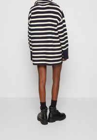 Pull en maille rayé bleu marine et crème à coupe décontractée, avec un col à revers et des manches longues, associé à des bottes noires épaisses.