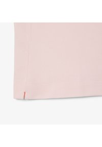 Ljusrosa T-shirt med en texturerad tyg, som har en sidoöppning vid fållen och en liten korallaccent vid nederkanten.