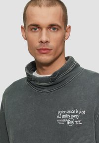 Grijze katoenen sweatshirt met een hoge kraag, met witte tekst "de ruimte is slechts 62 mijlen verderop" en een logo aan de voorkant.