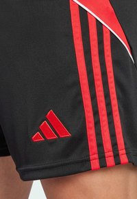 Sorte træningsshorts med røde sidestriber og hvide detaljer, prydet med et struktureret rødt Adidas-logo på venstre ben.