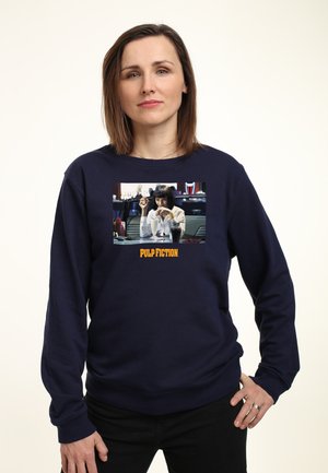 Granatowy sweatshirt z centralnym graficznym wizerunkiem kobiety, z tekstem "PULP FICTION" w pomarańczowym poniżej, wykonany z materiału z mieszanką bawełny.