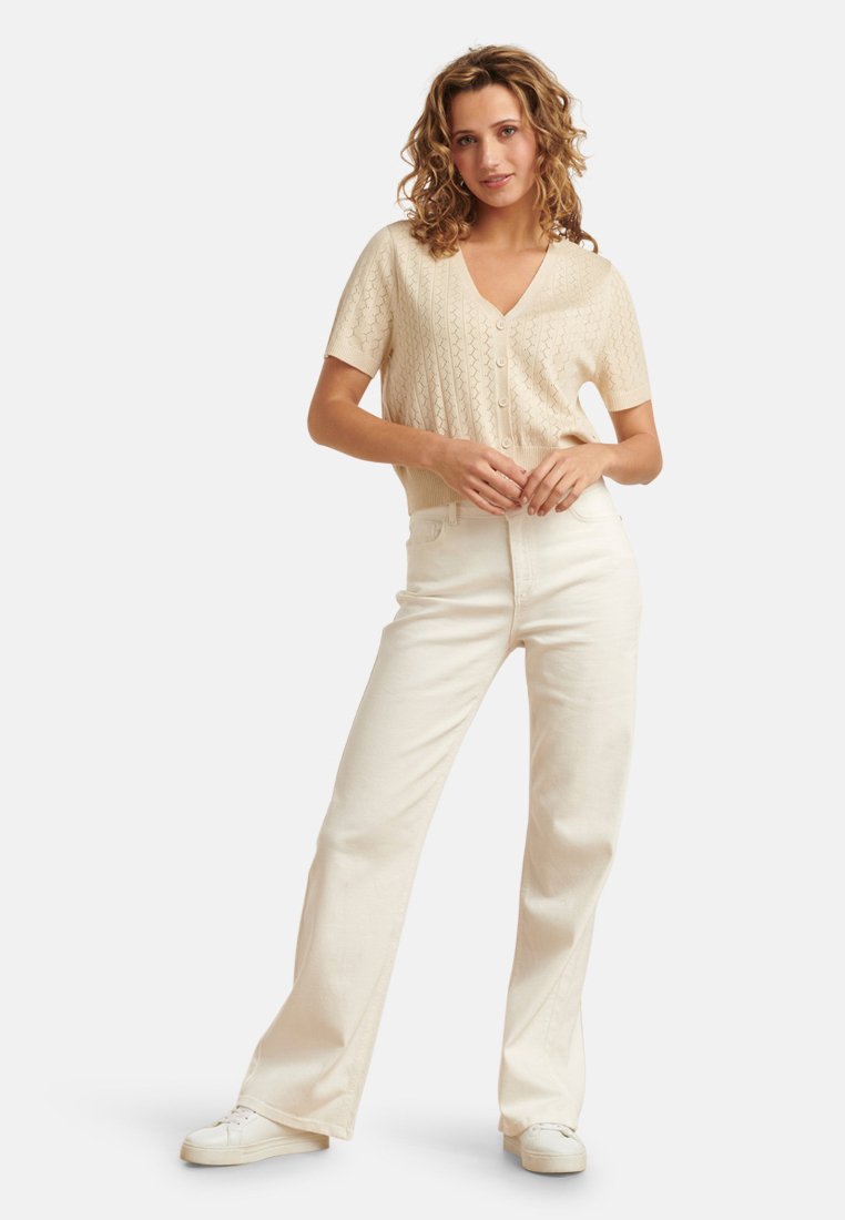 Beige gebreide cardigan met korte mouwen en V-hals, met knoopsluiting, gecombineerd met off-white recht passende jeans en witte sneakers.
