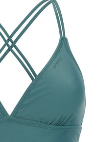 Türkisfarbener Bikinioberteil mit dünnen doppelten Trägern, die sich am Rücken kreuzen, und dem "protest"-Logo, das nahe dem oberen Rand der Körbchen gedruckt ist.