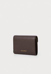 Portafoglio in pelle marrone a forma di pepite con logo dorato. Presenta un design pieghevole e una texture liscia, offrendo una forma rettangolare compatta.