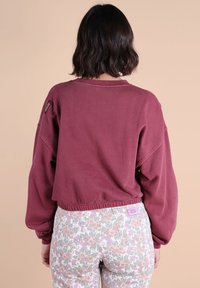 Sweatshirt court bordeaux à manches larges et ourlet élastique, associé à un pantalon à motif floral gris avec des accents roses et violets.