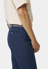 Heren navyblauwe broek gemaakt van stof met een gladde textuur. Heeft een achterzak en een geweven riem met een patroontje in blauw en wit.