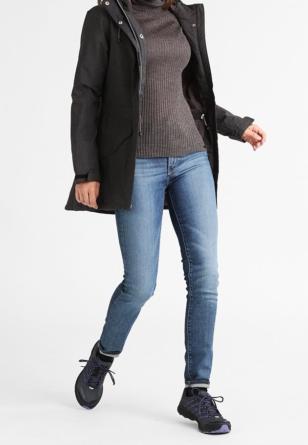 Veste imperméable noire avec capuche, pull côtelé gris, jean bleu et chaussures de sport noires avec des accents violets.