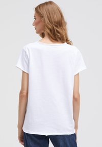 White short-sleeve t-shirt with a rounded neckline, soft texture, and a relaxed fit, paired with dark denim jeans.