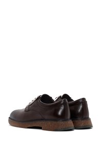Chaussures en cuir marron foncé à lacets avec des semelles en caoutchouc texturé, présentées en vue arrière en trois-quarts sur fond blanc.