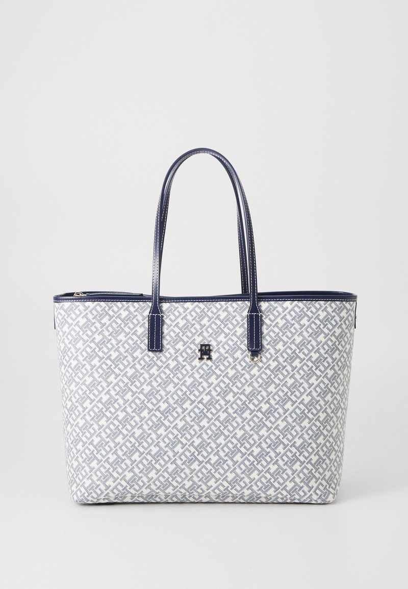 Grande borsa a spalla bianca e blu navy, con un motivo geometrico, texture liscia, due manici e chiusura a zip. Dettaglio del logo sul davanti.