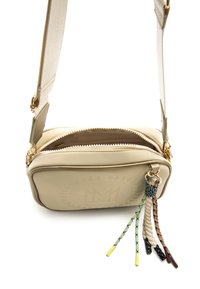 Bolso bandolera rectangular beige con cremallera dorada, que cuenta con un logo texturizado y borlas trenzadas de colores sujetas al tirador de la cremallera.
