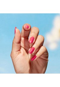 Heldere roze nagellak op vijf vingers, met een glanzende afwerking; verschillende tinten op elke nagel; hand gepositioneerd tegen een blauwe achtergrond.