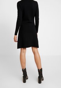 Schwarzes Strickkleid mit langen Ärmeln, tailliertem Oberteil und schwingendem Rock, kombiniert mit schwarzen ankle boots mit Absatz und strukturiertem Detail.