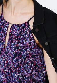 Granatowa bluzka w kwiatowy wzór w odcieniach fioletu, różu i zieleni. Posiada dekolt halter z wycięciem w kształcie łezki, w zestawieniu z czarną kurtką dżinsową.