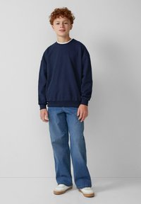 Felpa blu navy con una vestibilità comoda, scollo a girocollo e polsini a coste, abbinata a jeans chiari a palazzo e sneakers bianche.