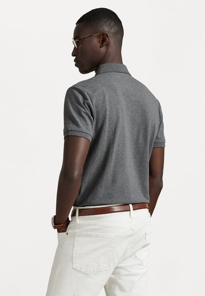 Γκρίζο πόλο μπλουζάκι με κοντά μανίκια, ύφασμα από βαμβακερό μείγμα και κλασικό γιακά. Συνδυασμένο με λευκά παντελόνια και καφέ δερμάτινη ζώνη.