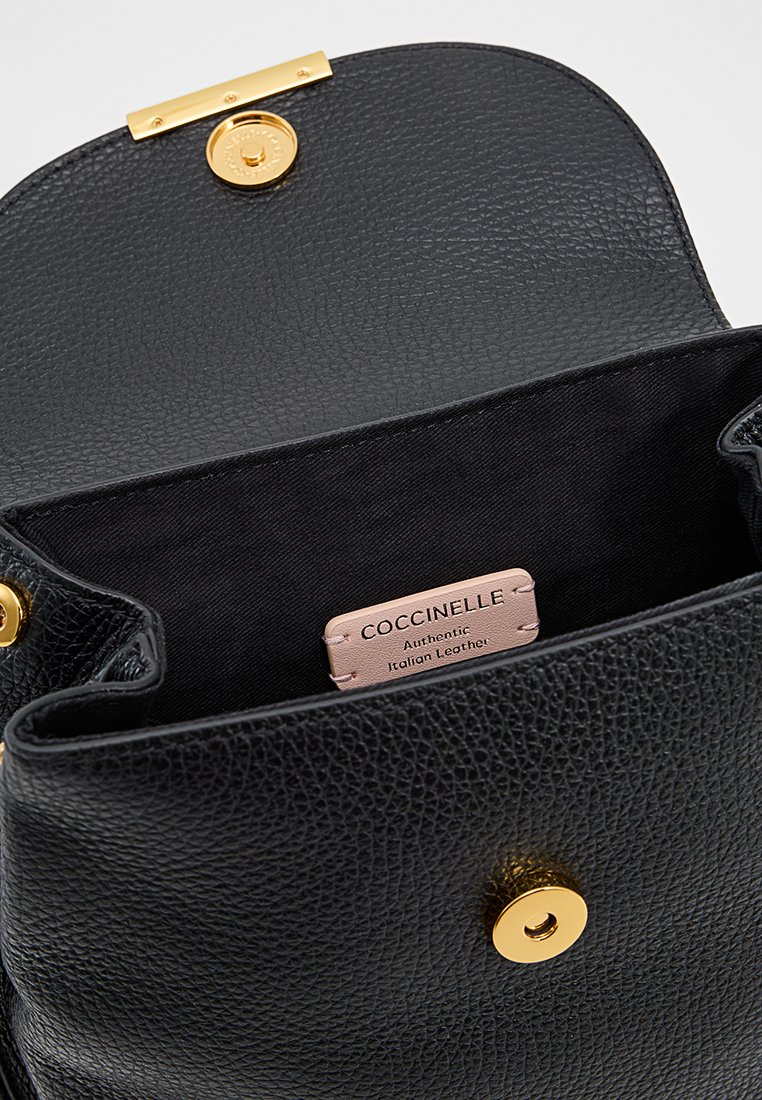 Czarna skórzana torebka z zapięciem w złotym odcieniu. Wnętrze wyłożone czarnym materiałem, z metką, na której widnieje napis "Coccinelle Autentyczna skóra włoska."