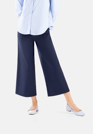 Navy wide-leg trousers made of smooth fabric, featuring a relaxed fit. Paired with light blue ballet flats with a minimal design and accent detail.