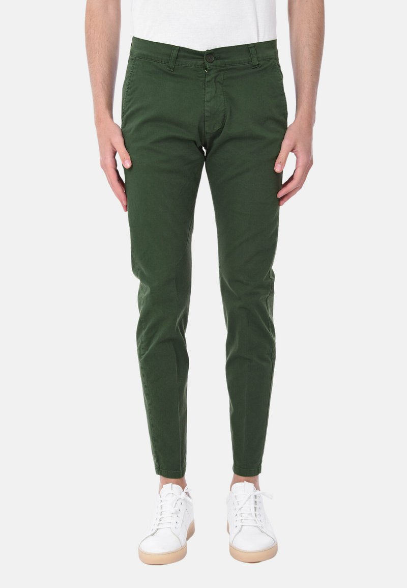 Chino in cotone verde con vestibilità slim, dotati di chiusura con bottone, passanti per cintura e gamba leggermente affusolata, abbinati a sneaker bianche.