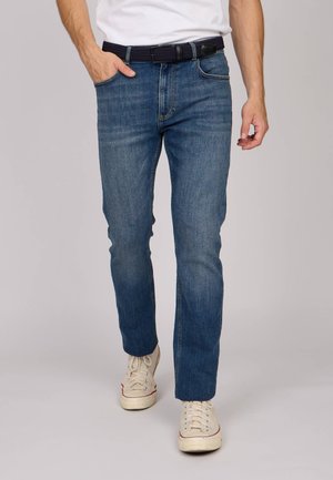 Jeans en denim bleu avec une coupe droite, comprenant cinq poches, un léger délavage et un ourlet surpiqué. Assortis à des baskets beiges et une ceinture noire.