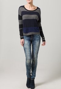 Randig tröja i grått, marinblått och svart med rundad halsringning och framficka, matchad med urblekta blå jeans och mörka ankelstövlar.