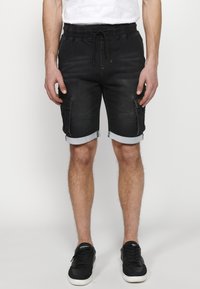 Pantalones cortos de carga de mezclilla negra con dobladillos enrollados, que cuentan con bolsillos laterales, una cintura ajustable con cordón y acentos de costura amarilla.
