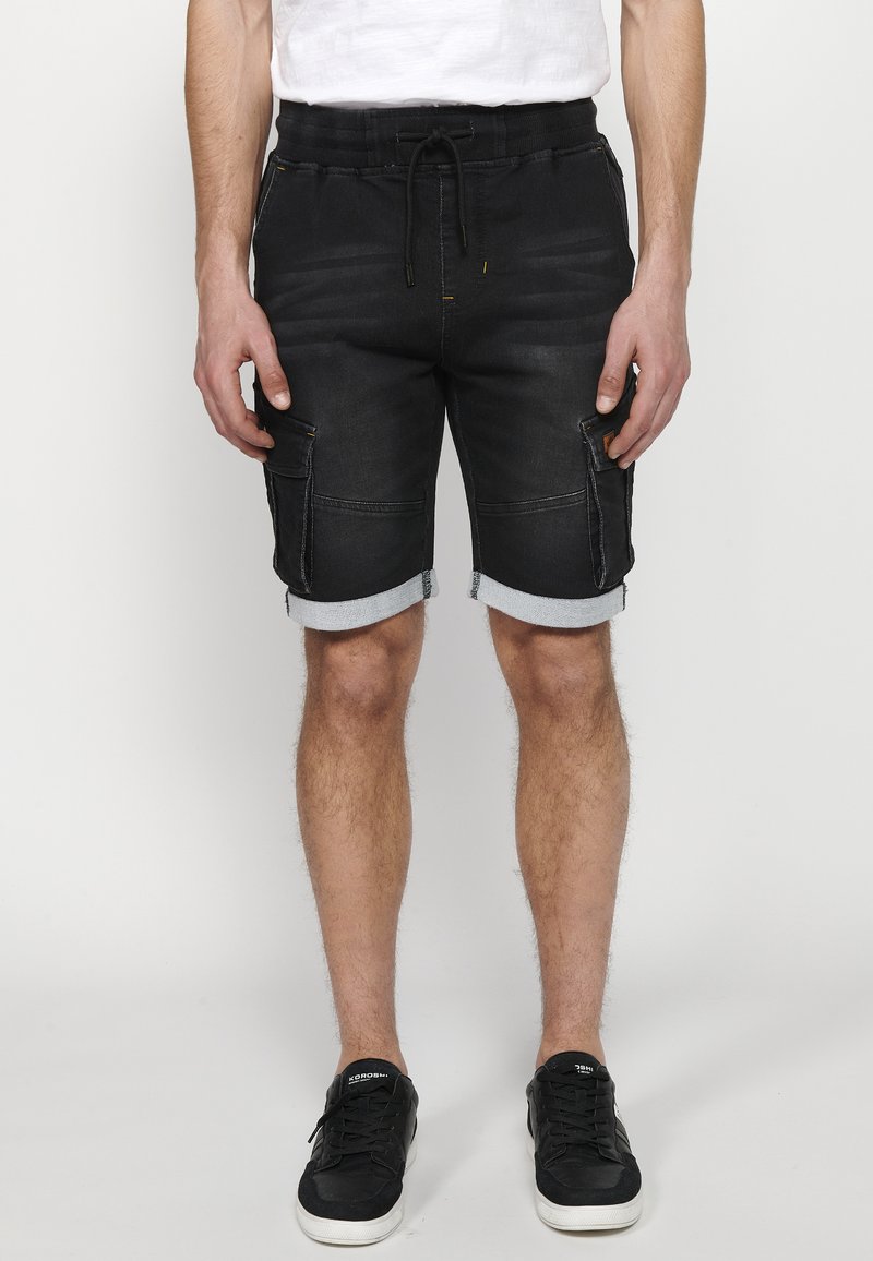 Pantalones cortos de carga de mezclilla negra con dobladillos enrollados, que cuentan con bolsillos laterales, una cintura ajustable con cordón y acentos de costura amarilla.