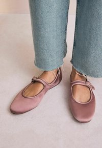 Ballerine in raso rosa Mary Jane con punta tonda, una fibbia decorativa sulla cinghia e una superficie liscia. Indossate con jeans azzurri sfilacciati.