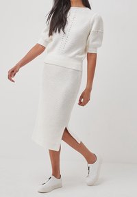 Ensemble en tricot blanc composé d'un haut à manches courtes et col rond, associé à une jupe mi-longue avec fente sur le côté, le tout agrémenté de baskets blanches.
