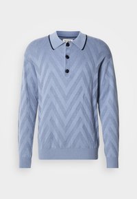 Polo tricoté bleu clair avec un motif en chevron, trois boutons noirs et un col marine contrastant. Manches longues et poignets côtelés.