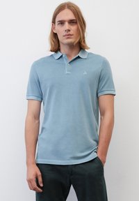 Helles blaues Poloshirt aus weichem Stoff, mit klassischem Kragen, kurzen Ärmeln und einem kleinen gestickten Logo auf der Brust.