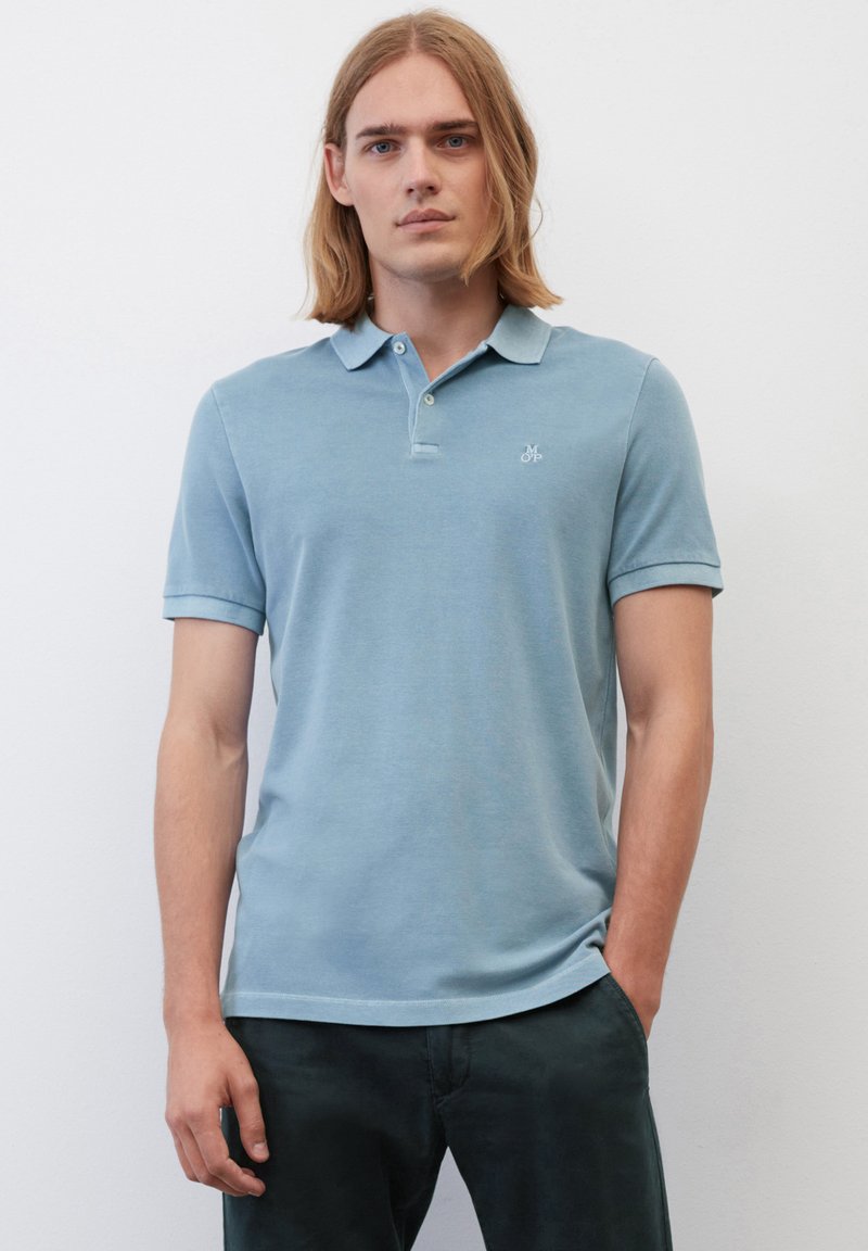 Helles blaues Poloshirt aus weichem Stoff, mit klassischem Kragen, kurzen Ärmeln und einem kleinen gestickten Logo auf der Brust.