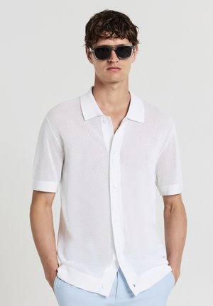 White short-sleeve shirt made of mesh fabric, featuring a button-up front, a classic collar, and rolled cuffs. Solid light blue pants.