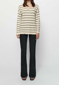 Karamell- och svartrandig stickad tröja med V-ringning, kombinerad med svarta utsvängda jeans och svarta klacksandaler. Texturerad och avslappnad passform.