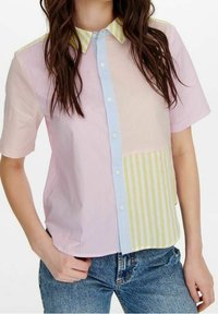 Chemise à manches courtes, à boutons, présentant des rayures roses, bleues et jaunes, avec des motifs verticaux et horizontaux contrastants et un col pointu.