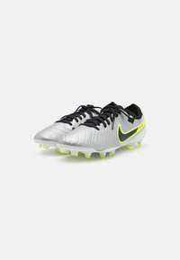 Sølv fodboldstøvler med struktureret syntetisk overdel, sorte snørebånd og et markant grønt og sort Nike-swoosh på siden. Gule studs på sålen.