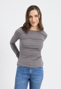 Gray long-sleeve top with a scoop neckline and gathered detail on the side, made from a fitted, smooth fabric. Paired with blue denim jeans.