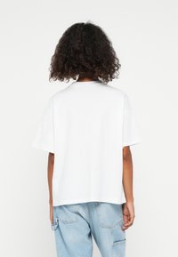 White cotton t-shirt with a loose fit, short sleeves, and a round neckline, paired with light blue denim pants.