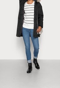 Sort polstret parka med en huva foret med pels, hvidstribet sweater, blå skinny jeans og sorte ankelstøvler med en glat tekstur.