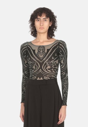 Long-sleeve mesh top in dark green with intricately patterned graphics. Features a round neckline and fitted design. Paired with high-waisted black trousers.