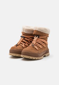 Brune semskede vinterstøvler med beige kunstpelskanter, oransje og svarte mønstrede snørebånd, og lette gummisåler med rillede detaljer.