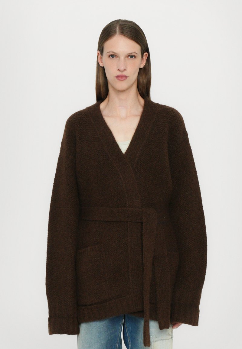 Brown, textured cardigan with a wrap design, long sleeves, and a tie belt. Features two front pockets and a relaxed fit.