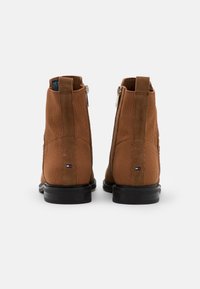 Stivaletti alla caviglia in camoscio marrone con chiusura a zip, tessuto testurizzato e suola in gomma nera. Presentano un piccolo logo sul tallone.