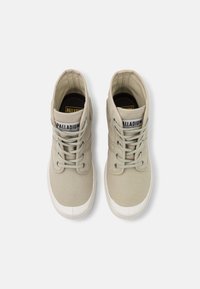 Sneakers alta in tela color beige chiaro, con punta in gomma bianca, chiusura con lacci e logo impresso sulla linguetta e sul lato.
