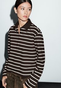 Polo a maniche lunghe a righe marroni e bianche con colletto, caratterizzato da una vestibilità comoda, patta con bottoni e texture di tessuto morbido.