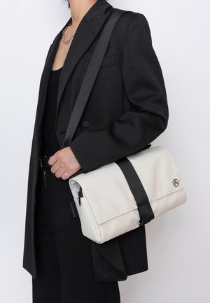 Crossbody-Tasche aus strukturiertem cremefarbenem Material mit einem schwarzen Tragegurt. Verfügt über eine magnetische Klappenöffnung und ein Logo an der Seite.
